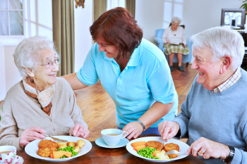 caregiver serving meal to senior couple